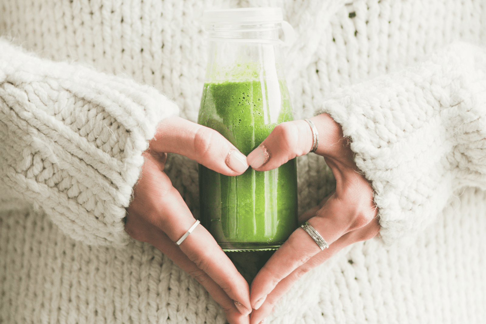 Hands forming a heart shape around a bottle of green smoothie