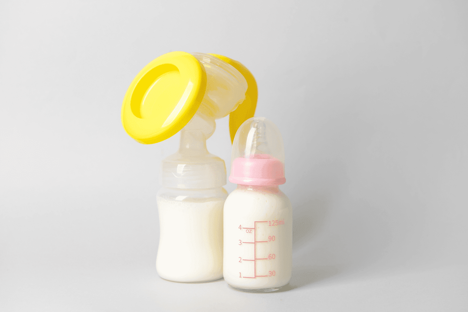 Breast pump and baby bottle filled with expressed breast milk on a plain background.