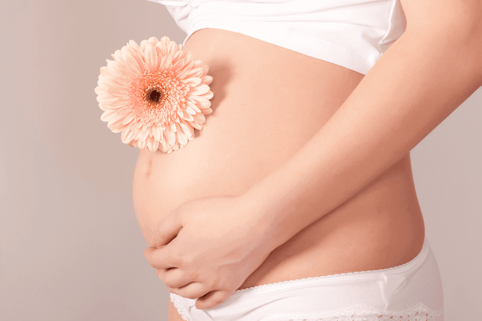 Pregnant belly with hands gently holding it and a pink flower placed on top