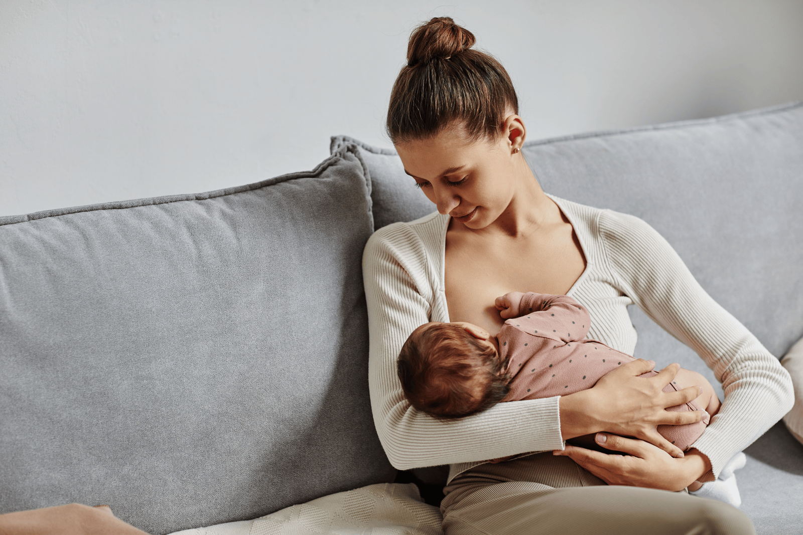 Mother seated on a sofa, cradling and breastfeeding her baby