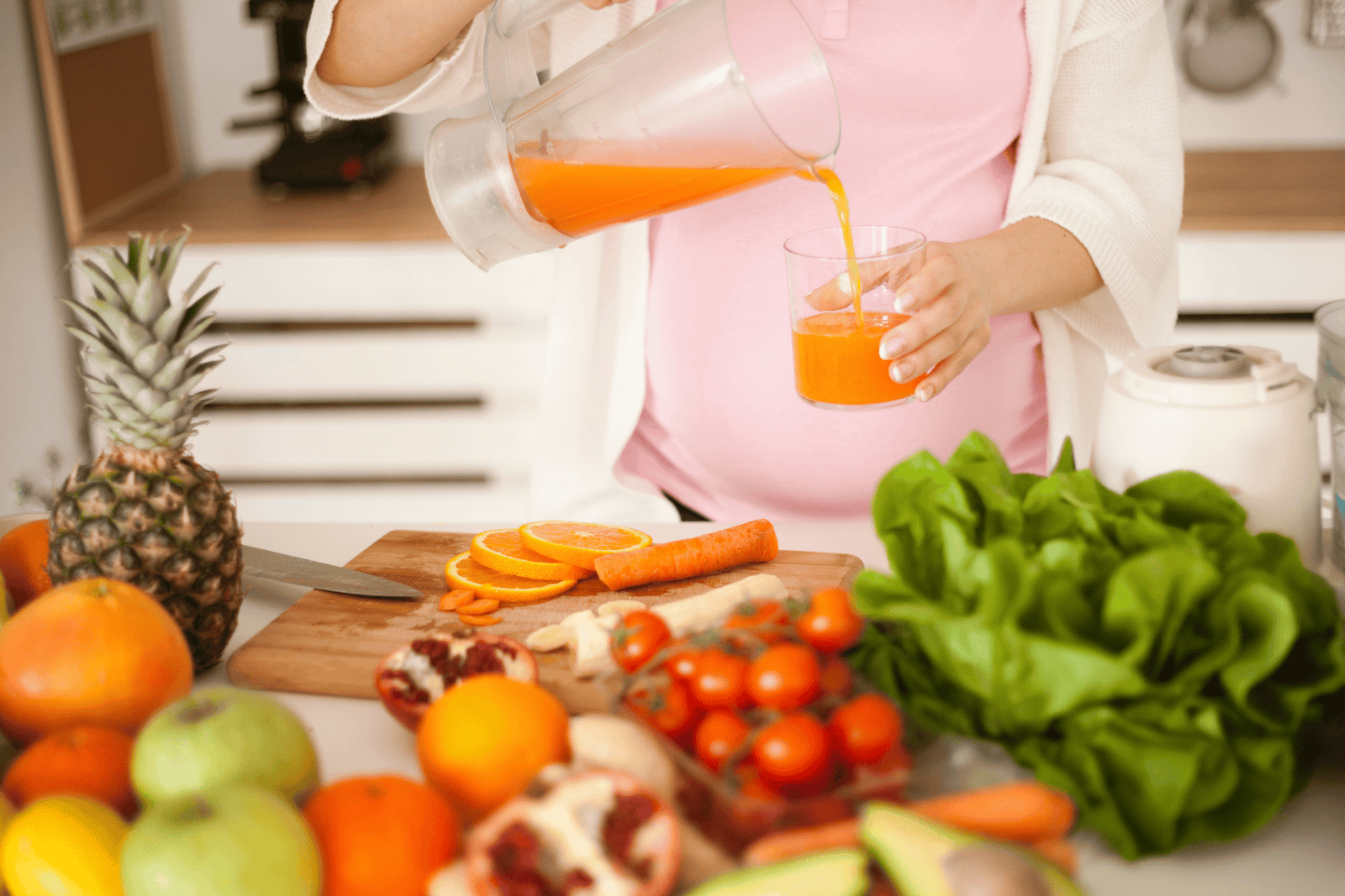 Person pouring fresh orange juice into a glass in a kitchen surrounded by fruits and vegetables