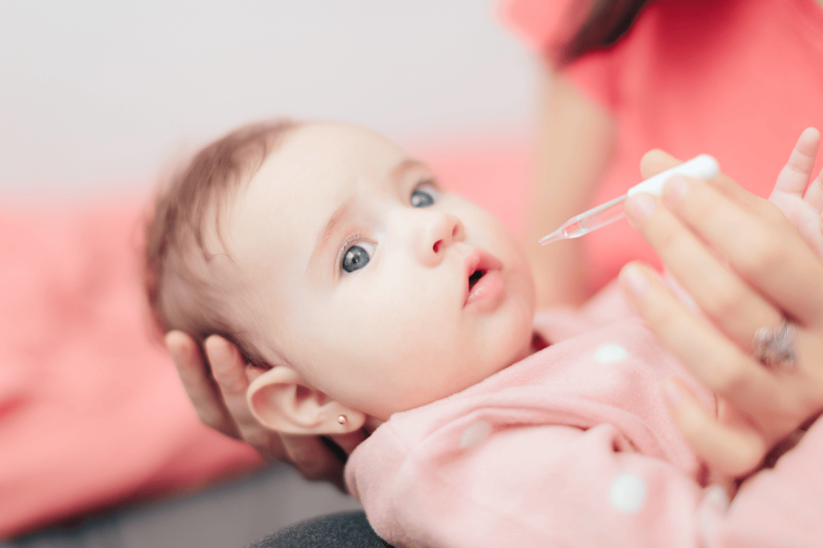  A caregiver gently holding an infant while administering liquid medicine or vitamin drops with a dropper, with the baby looking up attentively.