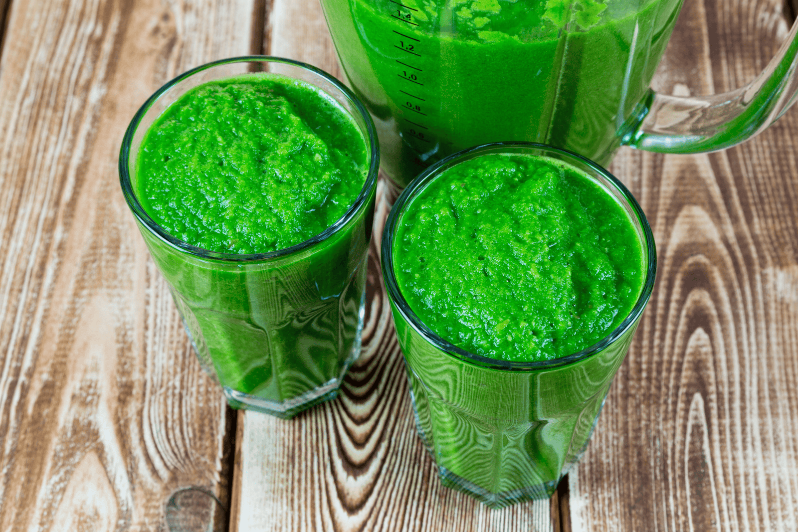 Green smoothies in glasses next to a blender on a wooden table