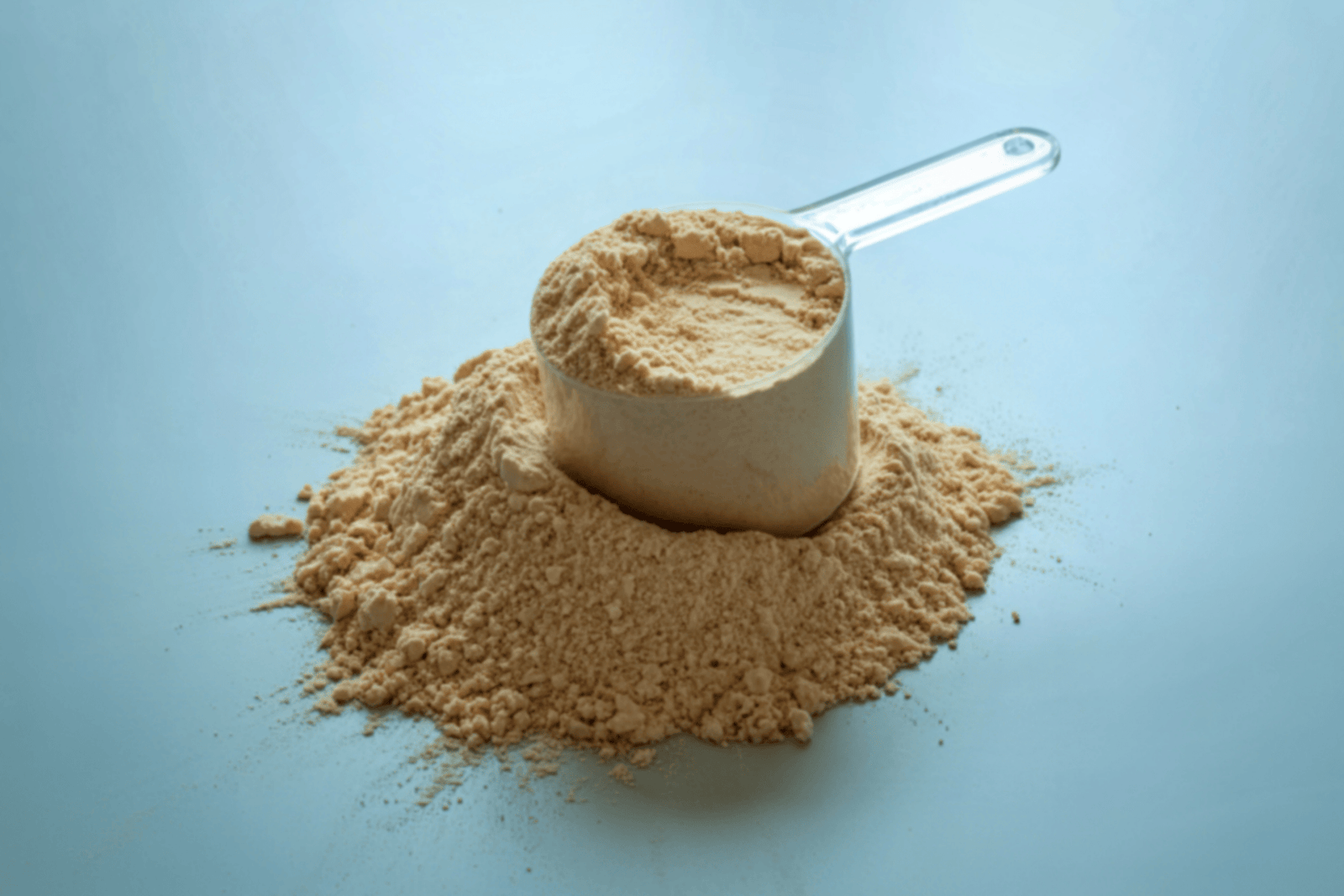 Scoop of sunflower lecithin powder on a light blue surface.