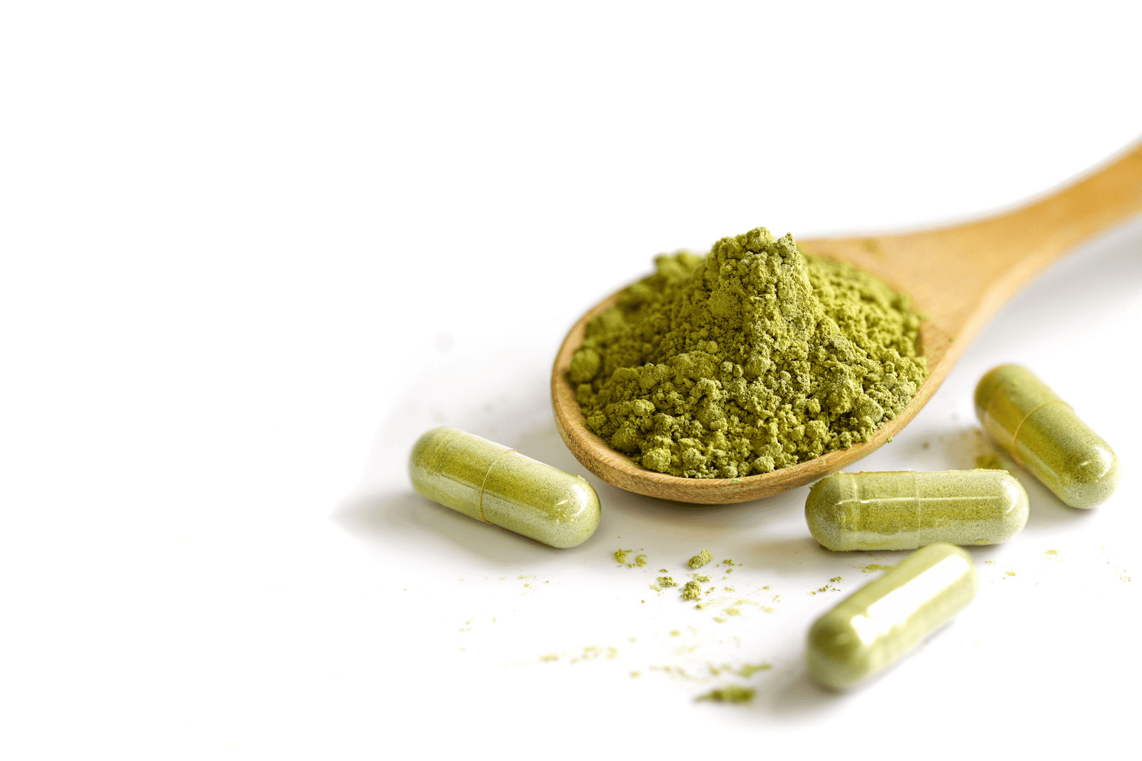 Green superfood powder in a wooden spoon with capsules on a white background.