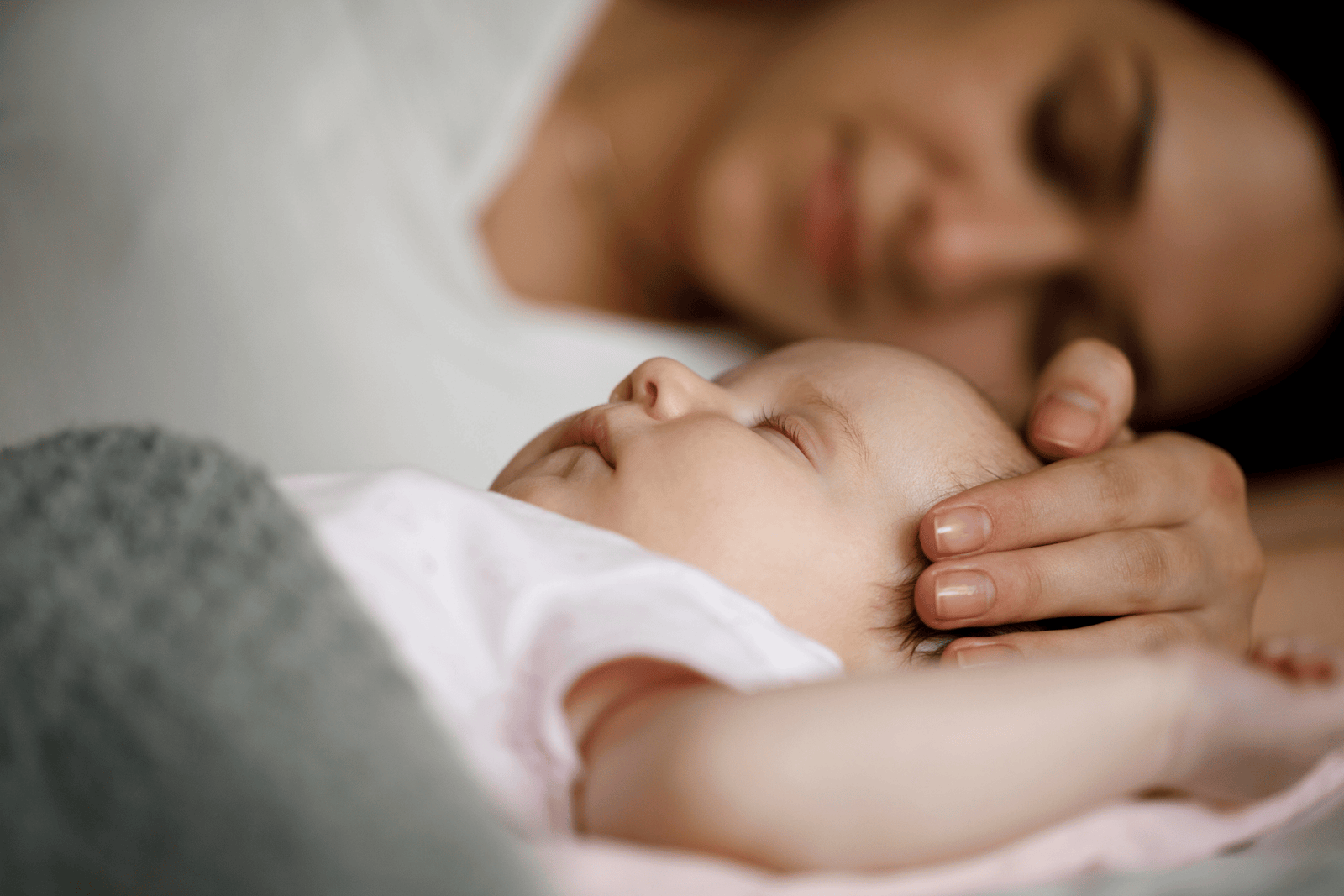 Mother resting peacefully beside her sleeping baby, gently cradling the infant's head.