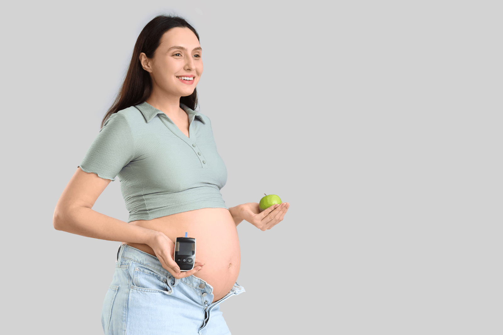 Pregnant woman holding a green apple and a blood glucose meter, symbolizing gestational diabetes management and healthy pregnancy nutrition.