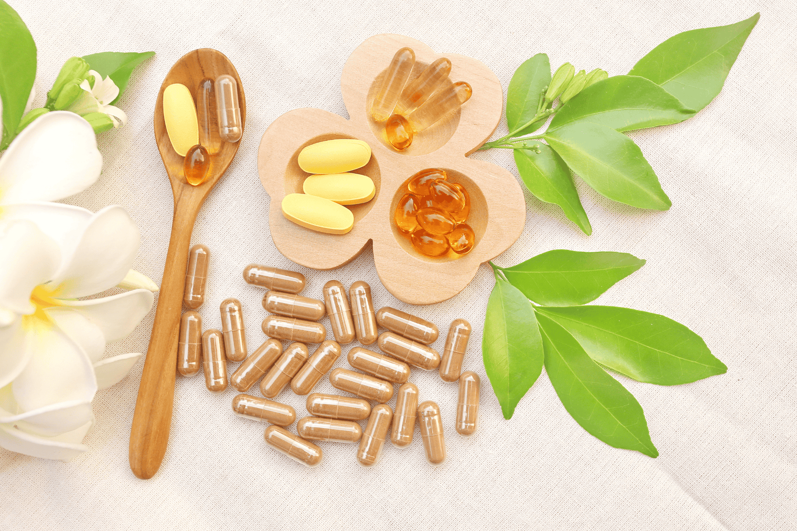 Assortment of supplements and capsules arranged with leaves and flowers on a light fabric background.