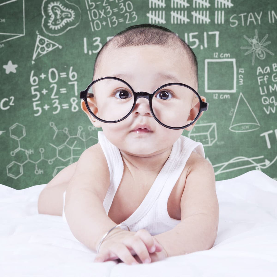 Bebé con lentes frente a un pizarrón